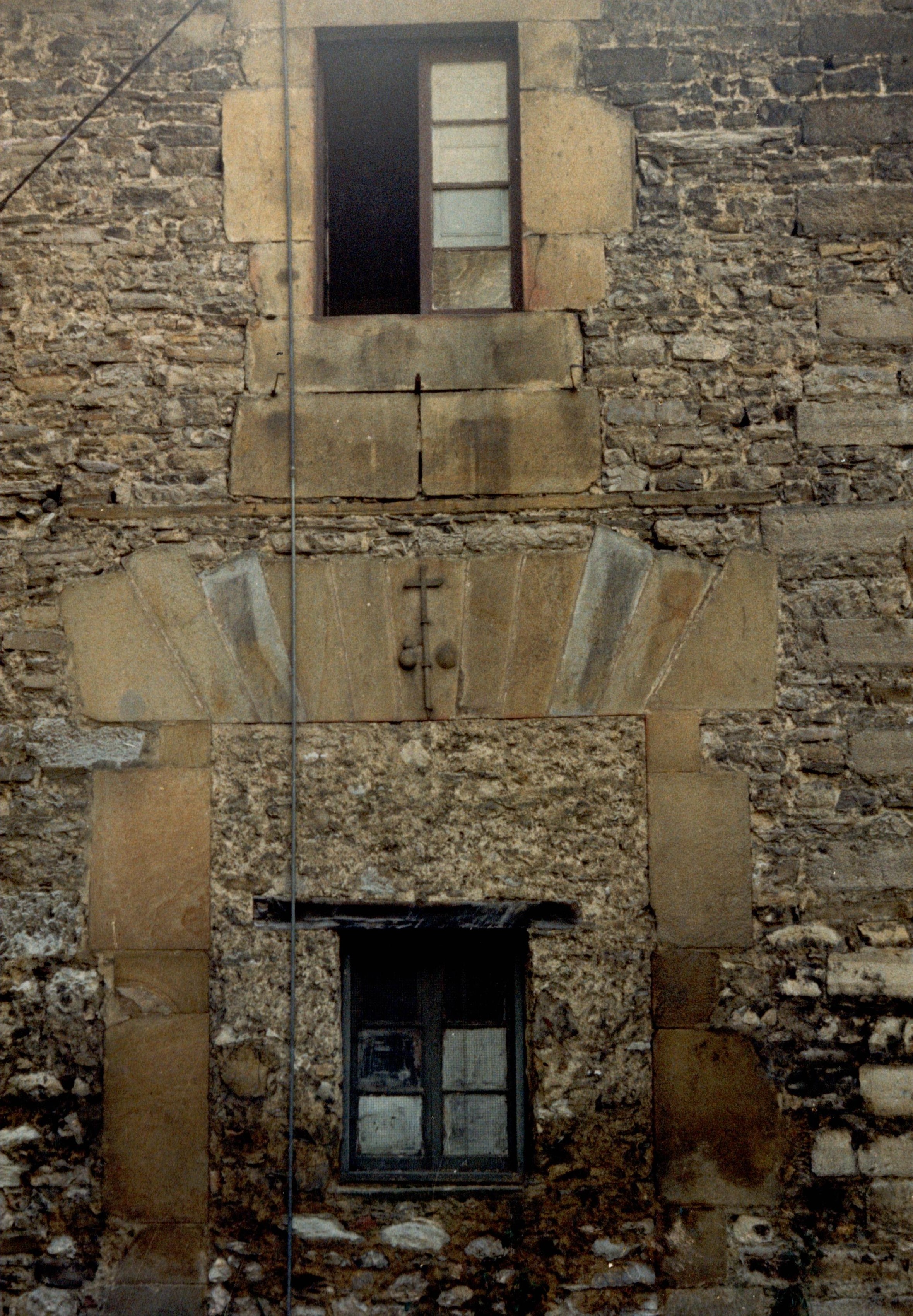 Se ve la fachada interior de un edificio, sin decoraciones y con piedra menos trabajada que en la fachada principal. Hay dos ventanas, una de ellas está medio abierta (solo una de las hojas).