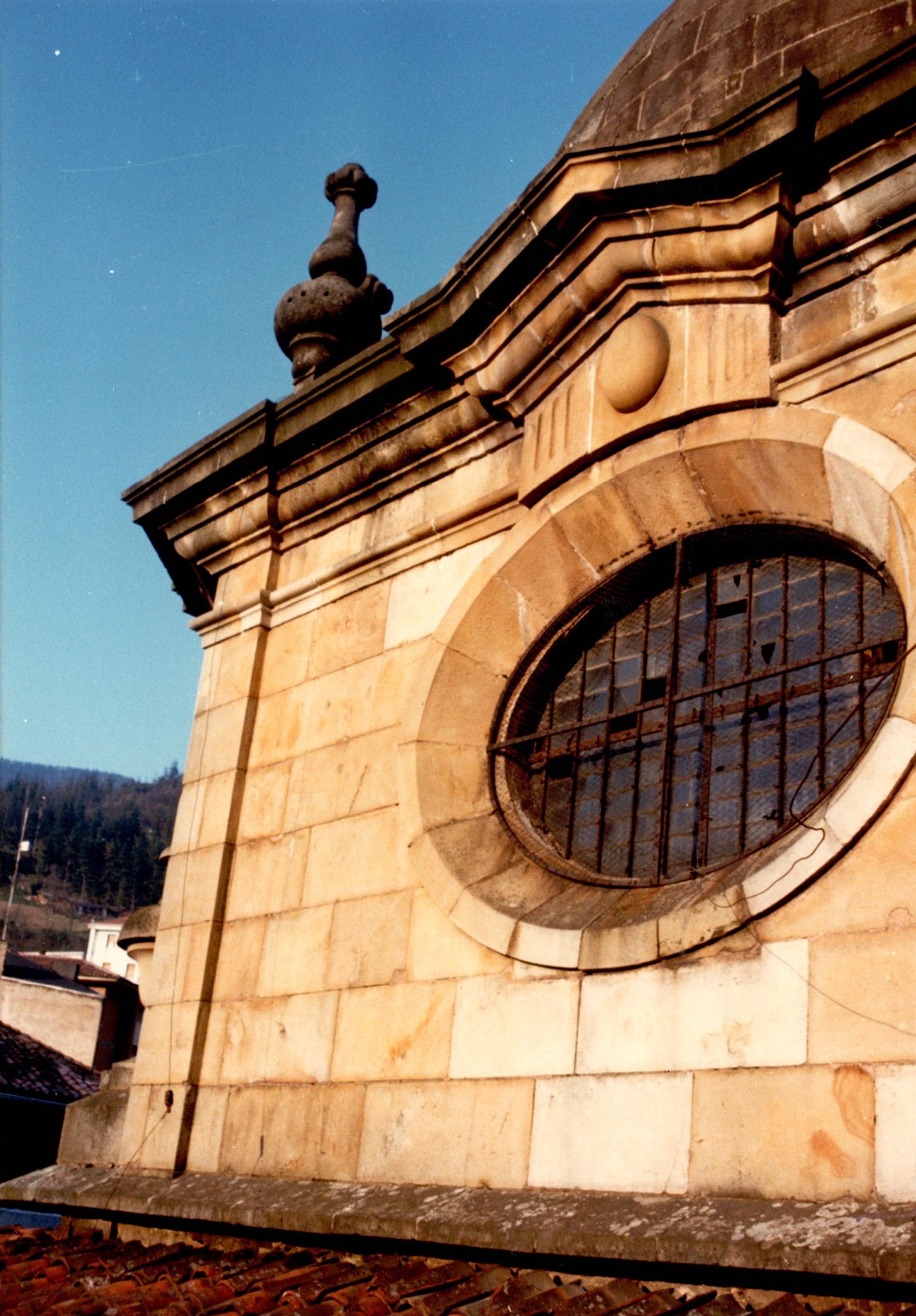 Se ve parte del tejado del edificio, de ladrillos rojos. También se ve la estructura que sostiene una cúpula, una ventana redonda y un pináculo