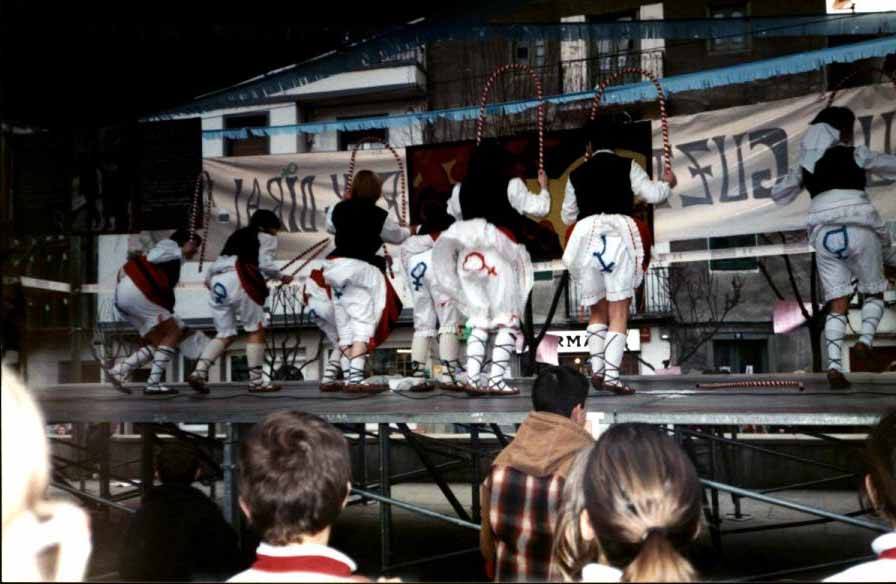 Unas ocho mujeres están sobre el escenario bailando o en movimiento al menos. En los pantalones tienen en azul algunas y en rojo otras el símbolo de la mujer pintado.