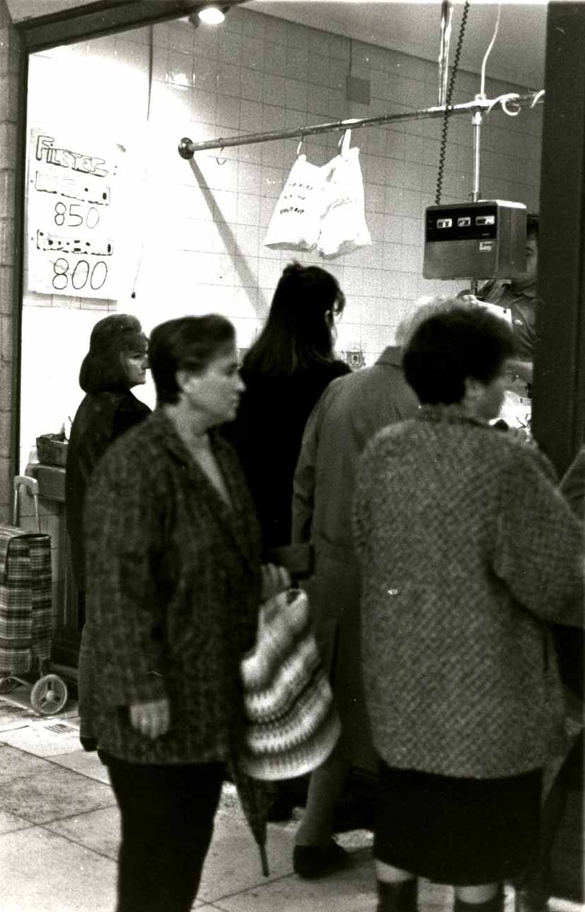 Cinco señoras están frente a uno de los puesto de la Plaza del Mercado esperando a ser atendidas. Fotografía en blanco y negro. A la izquierda se ve un cartel donde puede leerse "filetes". 