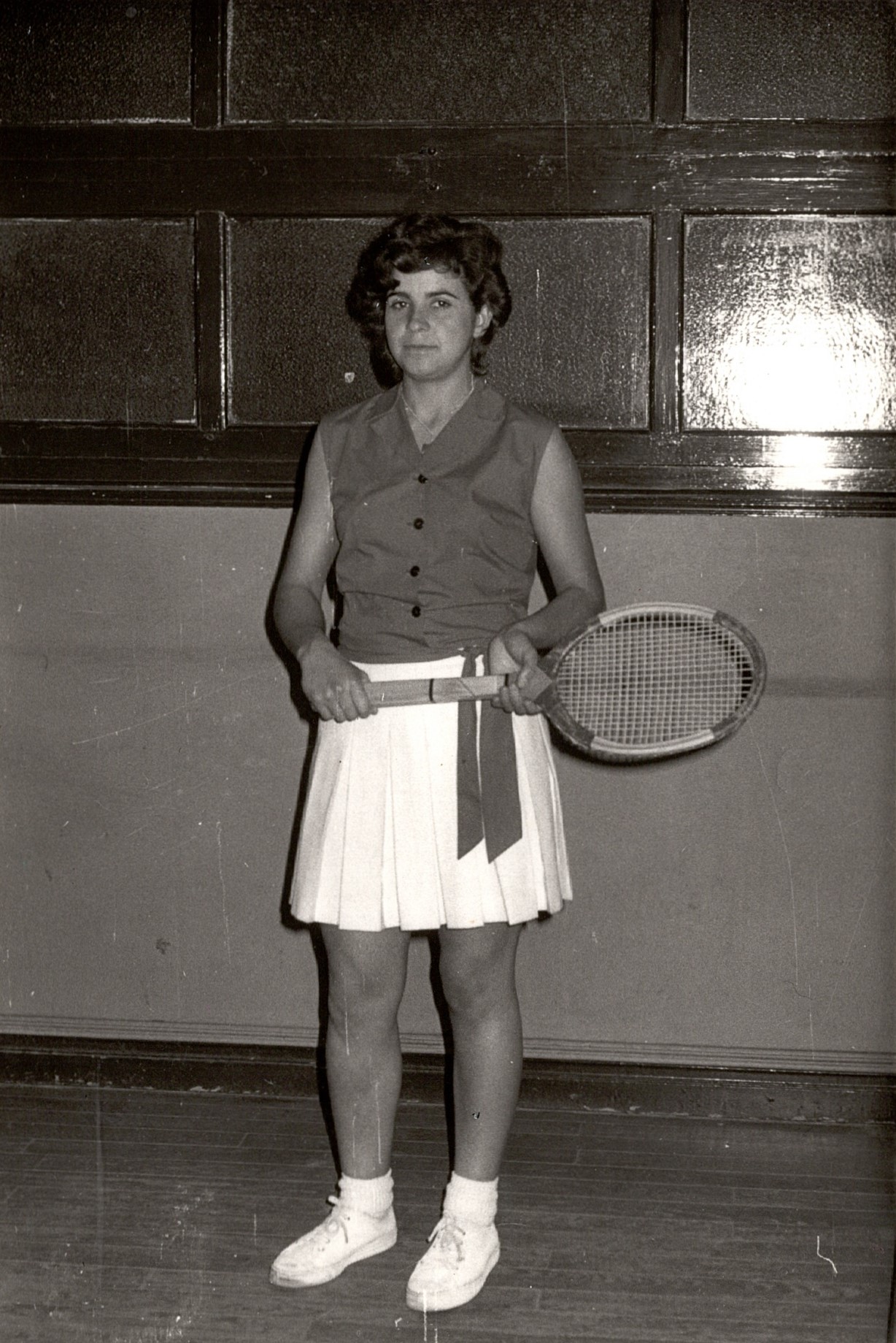 La raquetista Chari con la raqueta en la mano, fotografía en blanco y negro. Calza zapatillas deportivas, falda blanca y camisa de manga corta. 