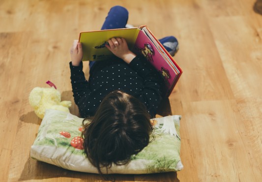 Niña leyendo un libro tumbada en el suelo